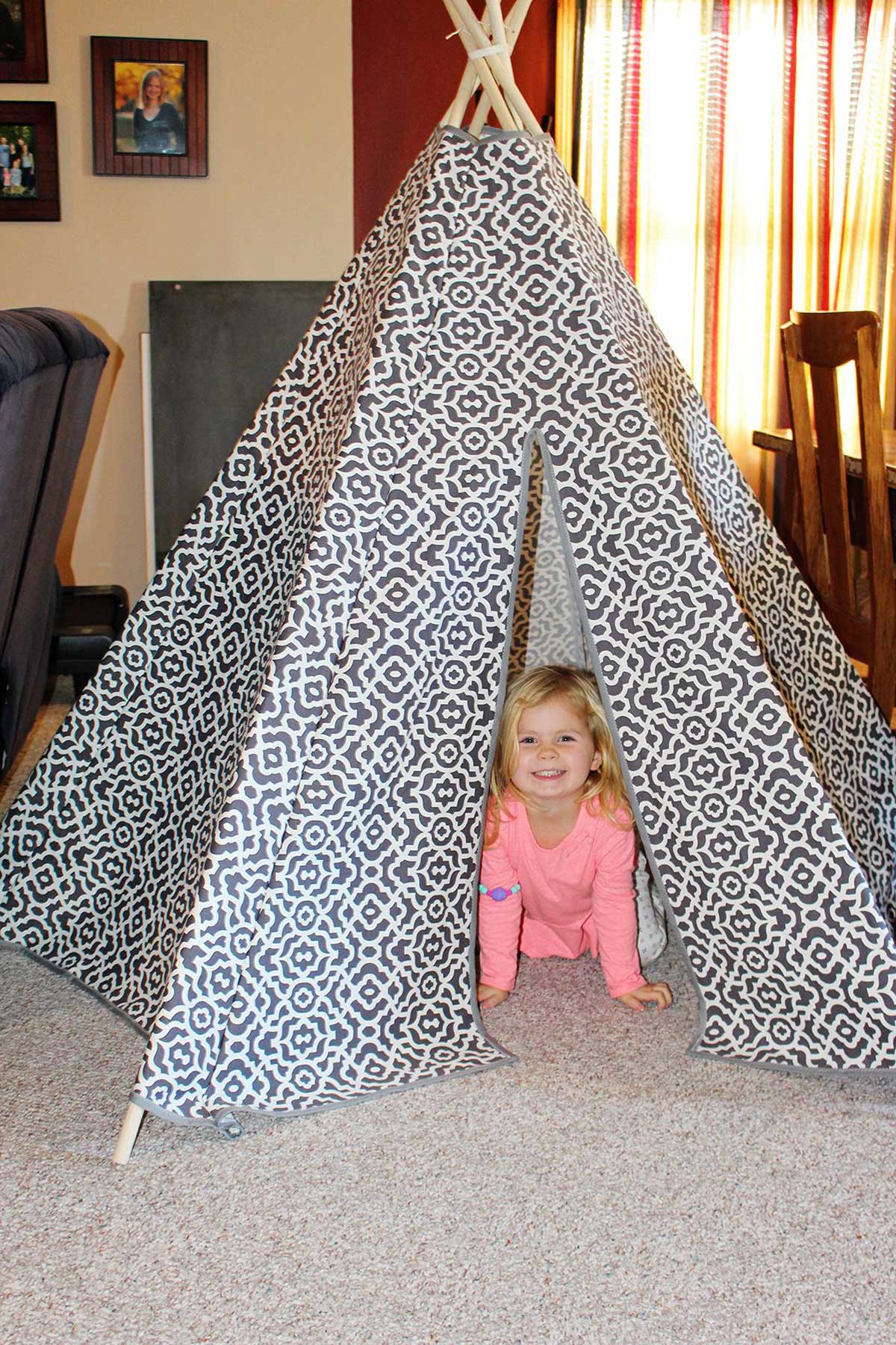 Uma criança pequena dentro de um toldo teepee DIY de tecido com estampas cinza e branca.