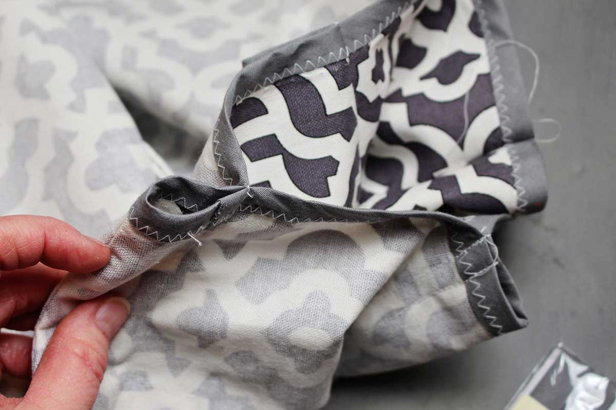 Tecido cinza e branco estampado com bordas finalizadas com fita viés cinza, costurado em um laço para segurar varas de madeira para fazer uma tenda teepee DIY.