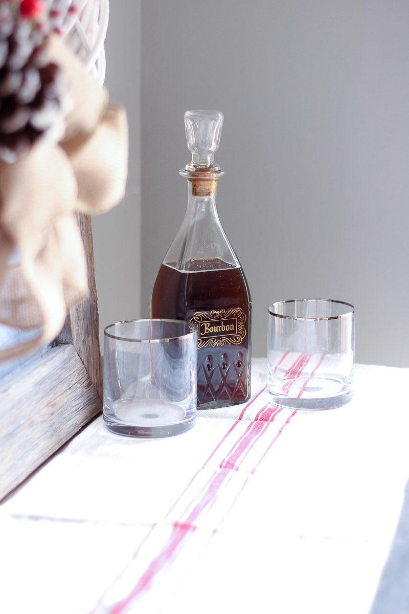 Decantador vintage de bourbon com copos de highball com borda dourada sobre um caminho de mesa de saco de grão vermelho e branco