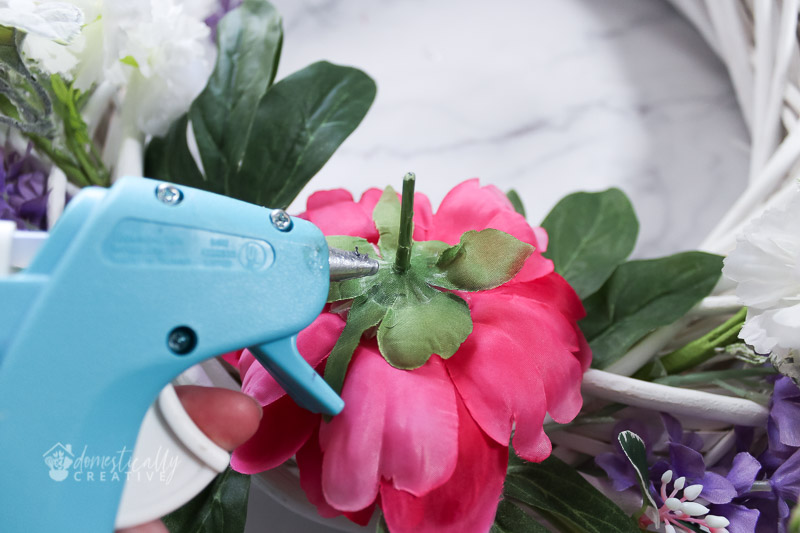 usando uma pistola de cola quente com flores de peônia para fixar na forma da guirlanda