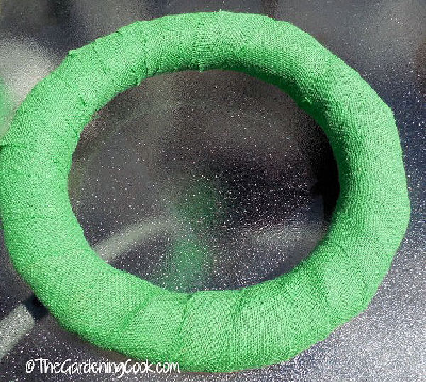 Uma forma redonda de guirlanda coberta com juta verde em uma mesa de vidro.
