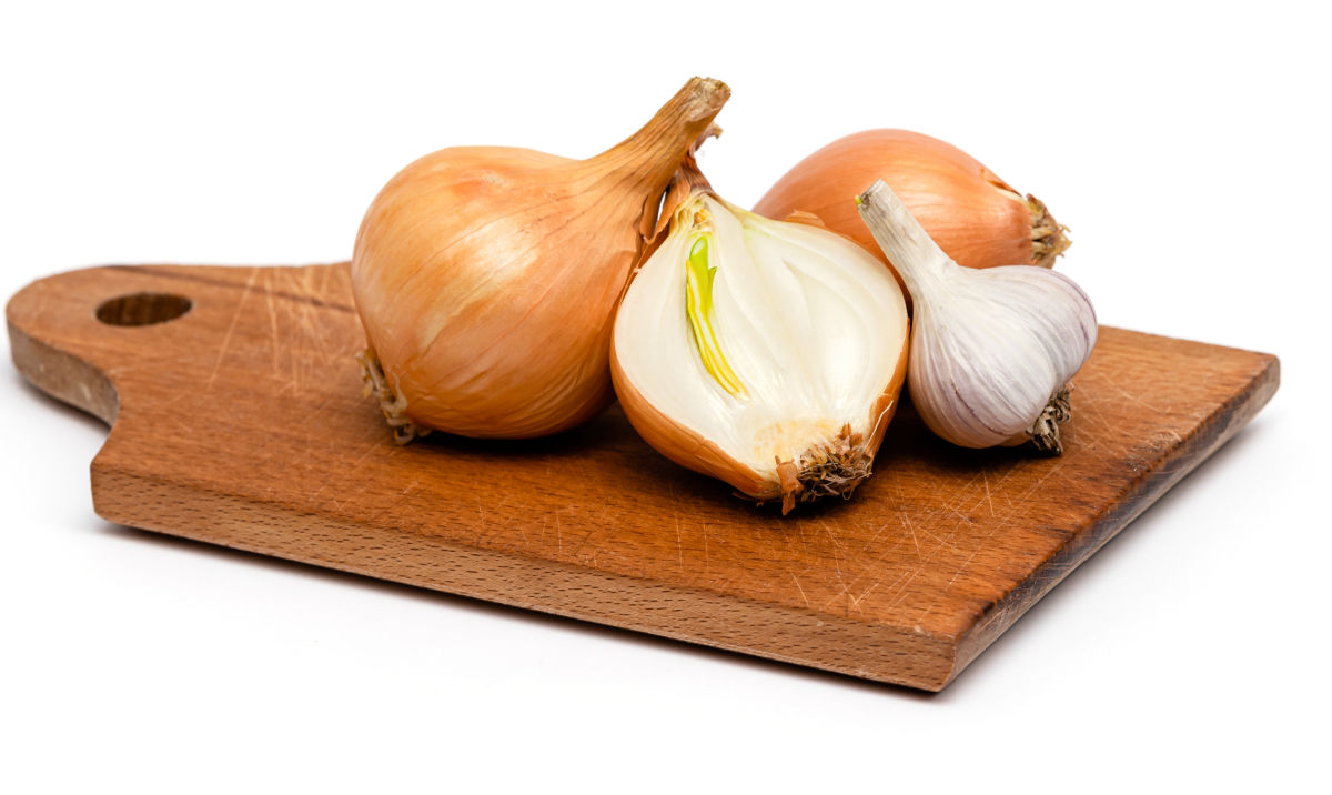 Cebolas amarelas e alho em uma tábua de corte de madeira para serem usados no lugar das chalotas em uma receita.